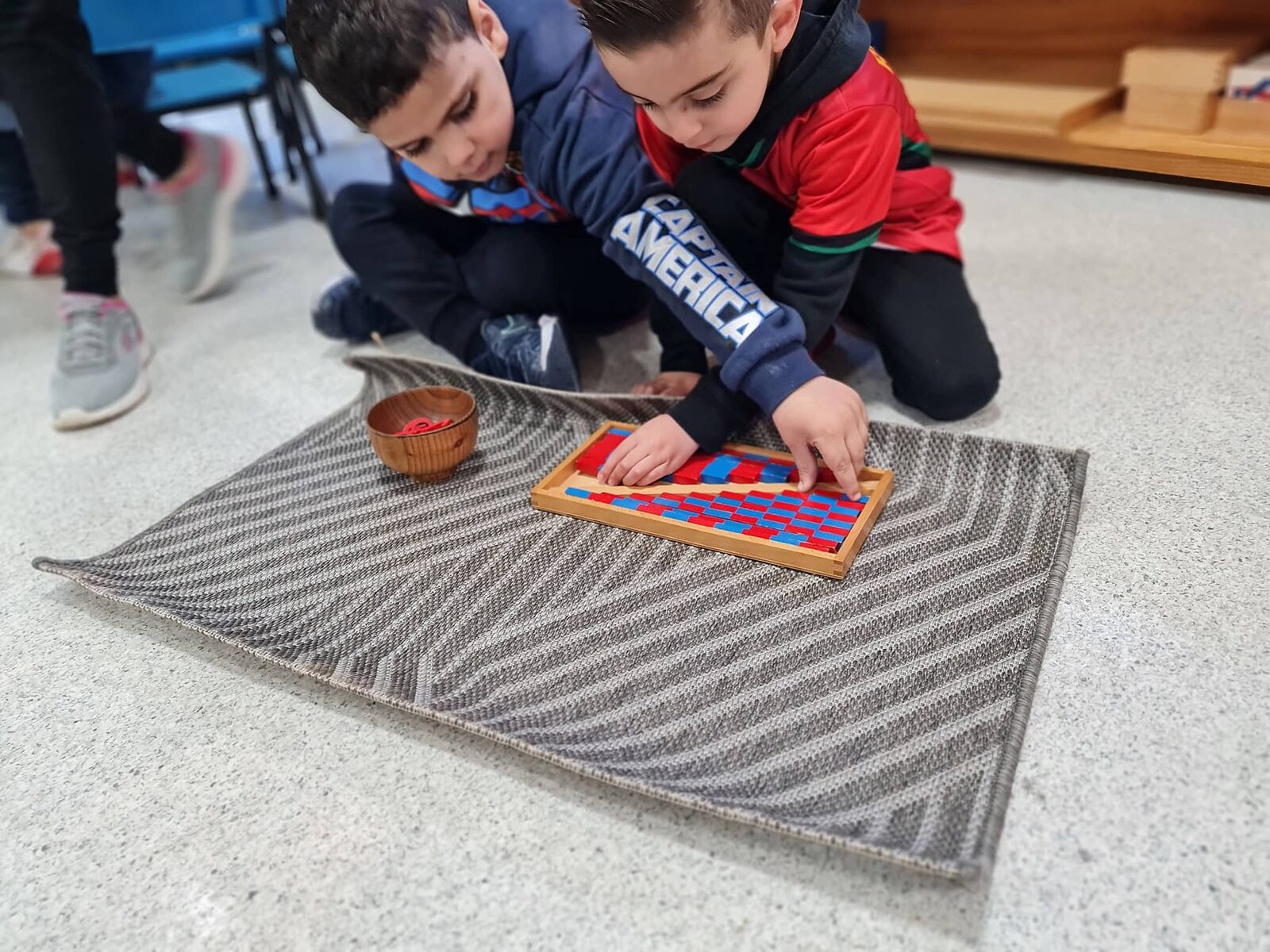 Two children working together with Montessori bead and rod materials on a floor mat
