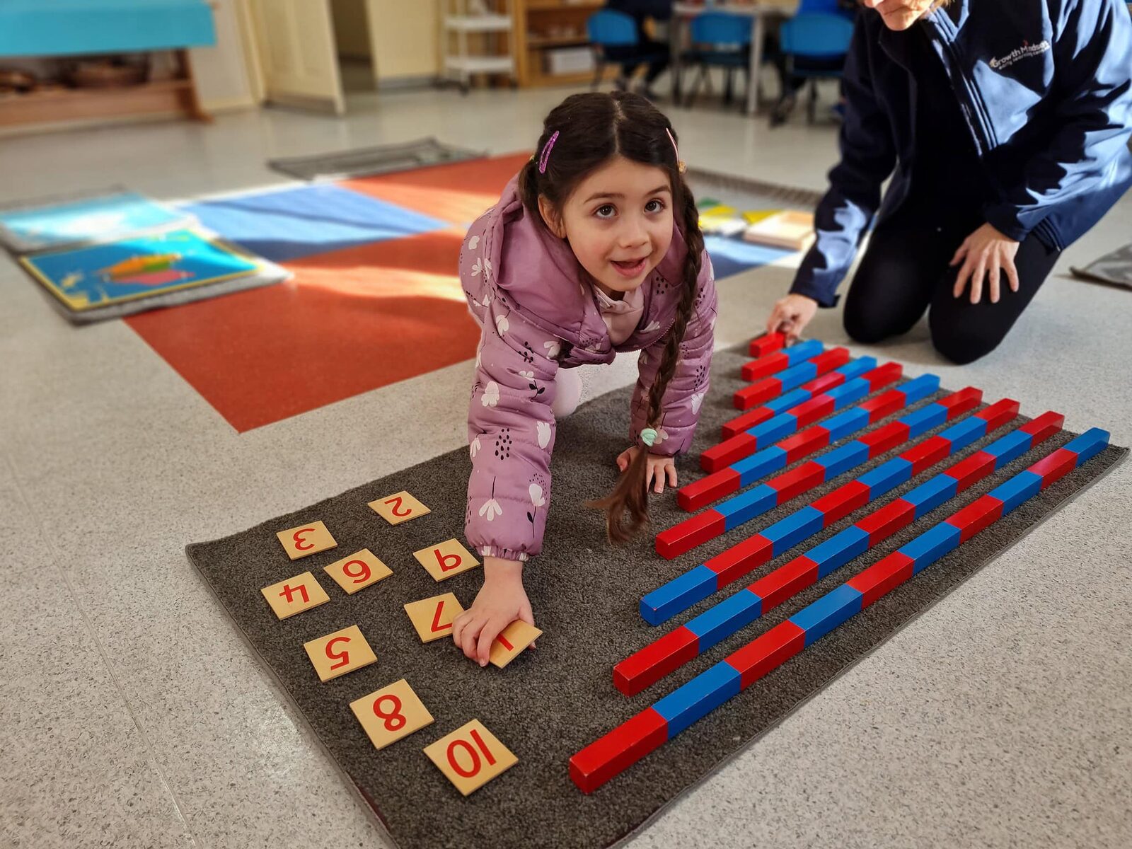 A preschooler laying out Montessori number rods and numerals with an educator